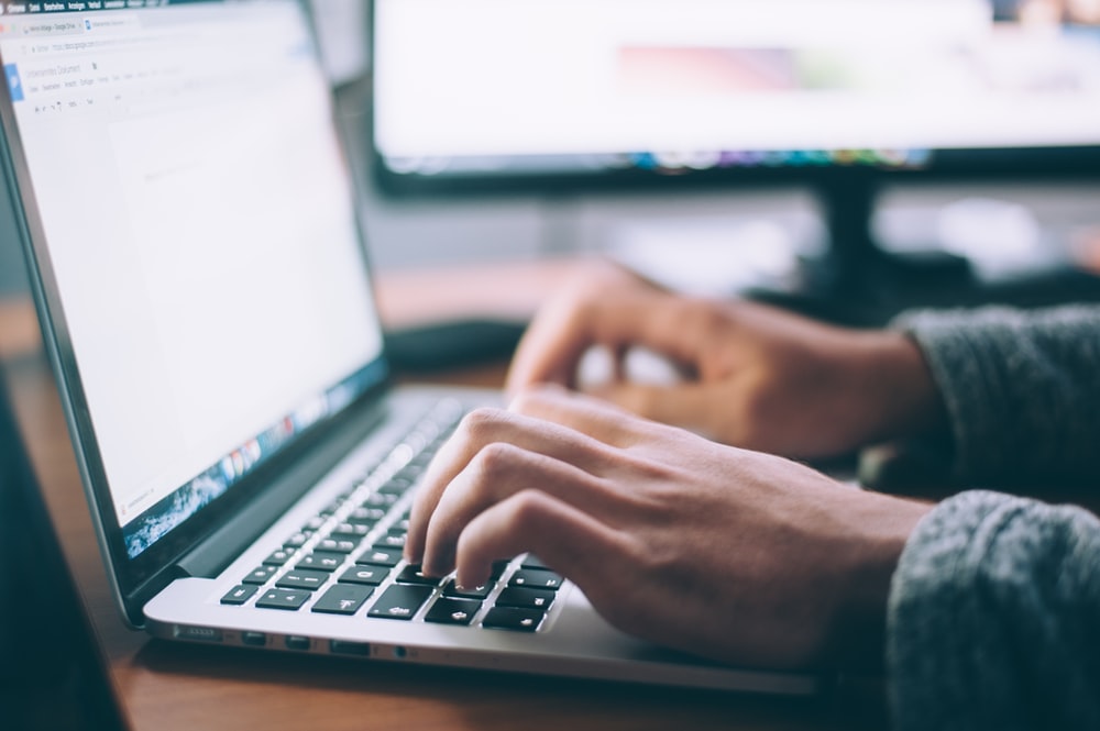 A unseen person's hands on a laptop, with a faded desktop in behind.